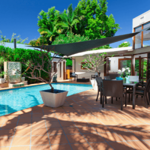 alt="Tropical South Florida backyard with a wood deck, sparkling pool, and wicker table with chairs."